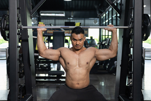 Asian Man Pumping Up Muscles with Weight Lifting Machine in a Gym