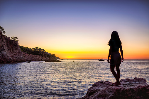 Silhouette of a young woman enjoying freedom over a rock in front of the sea waiting for the sun rise