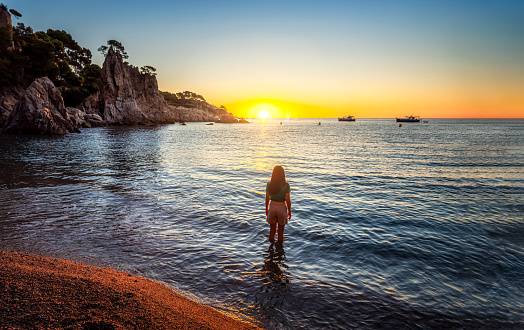 Woman enjoying the Sunrise in Costa Brava with the feet into the sea
