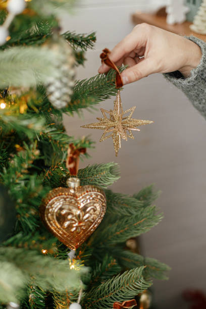 istock Hands decorating christmas tree with stylish bauble in atmospheric festive room. Merry Christmas! Winter holidays preparation. Woman in cozy sweater putting vintage star on tree 1434113577