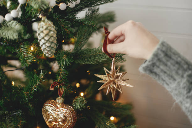 istock Hands decorating christmas tree with stylish bauble in atmospheric festive room. Merry Christmas! Winter holidays preparation. Woman in cozy sweater putting vintage star on tree 1434114345