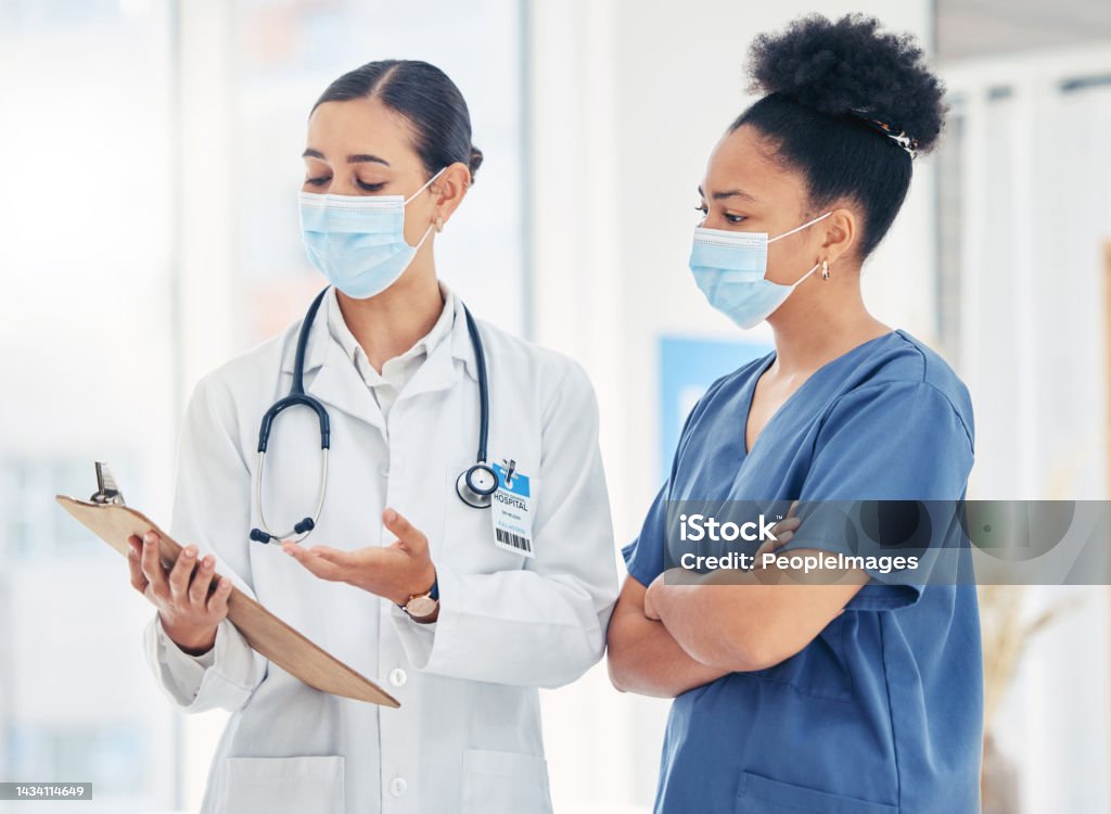 Doctor and nurse reading medical information paperwork with mask for safety from covid or corona virus in a hospital. Healthcare workers discuss and analyze pandemic data report in a clinic together Protective Face Mask Stock Photo