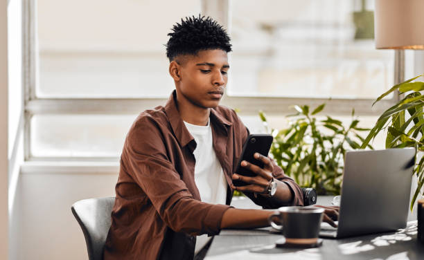 istock Smartphone, laptop and student man online course reading information, networking or reading social media post at home office desk. Gen z entrepreneur with multimedia technology for online website app 1434114743