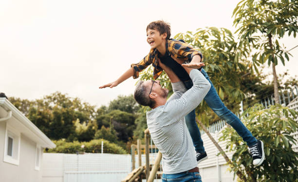 Man, kid and lift in air in garden, backyard or outdoor at house while play by trees, Father, boy and love while bonding, fun and happy time together at family, vacation or holiday in Orlando hombre, niño y ascensor en el aire en el jardín, patio trasero o al aire libre en la casa mientras juega junto a los árboles, padre, niño y amor mientras se unen, diversión y tiempo feliz juntos en familia, vacaciones o vacaciones en orlando