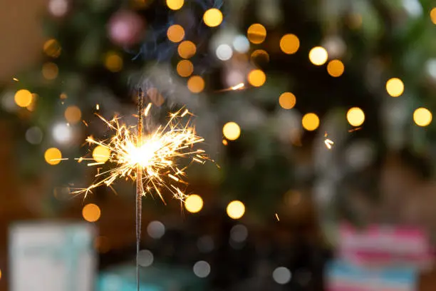 Photo of Christmas glittering sparklers candle burns in Christmas tree background. Xmas lighting decoration at home indoor. Festive Magic sparks lights for holiday party. Christmas eve with fireworks.