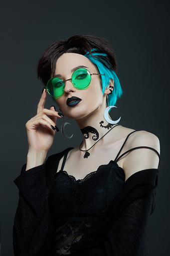 Beauty anime woman with short hairstyle in green glasses. Dyed hair, face makeup. Crescent moon earrings in the ear