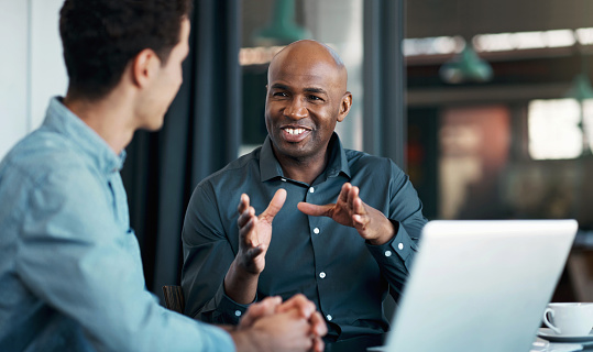 Happy black man, business and idea on laptop working with colleague explaining proposal at the office. Young African American in marketing strategy talking to employee at work for corporate ideas
