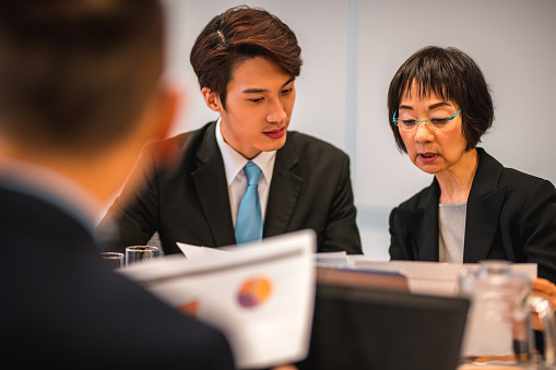 End of the day meeting at work. Over the shoulder shot of asian woman and man reading documents.