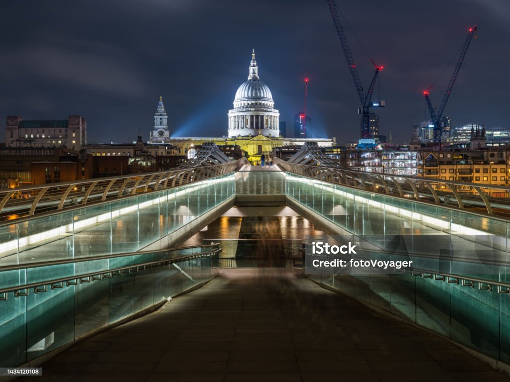 London St Paul's Cathedral dome spotlit over Millennium Bridge night The iconic dome of St. Paul’s Cathedral spotlit at night overlooking the futuristic glass and steel span of the Millennium Bridge crossing the River Thames in the heart of London, UK. Architectural Dome Stock Photo