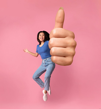 Cheerful Young Asian Lady Jumping In The Air And Showing Huge Thumb Up Gesture Over Pink Studio Background, Full Length Shot With Free Space, Creative Image For Gesturing Concept