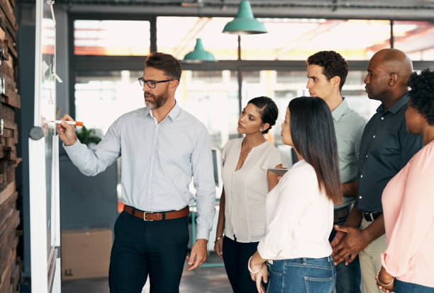 istock Man, ceo and manager with team presentation on whiteboard for coaching or training in global marketing company. Business people learning strategy, advertising, or sales from leader, speaker or mentor 1434121372