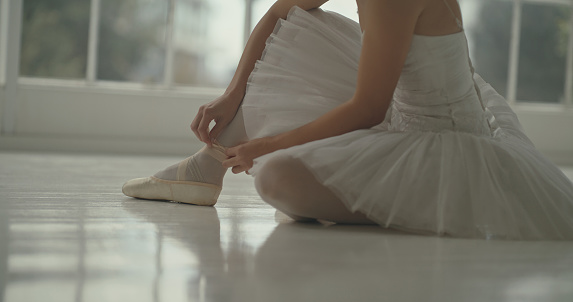 Ballet, floor and woman tie shoes for training, theater or competition. Ballerina, dancer and girl sitting in studio, getting ready for creative dance art or exercise for theatre, performance or show