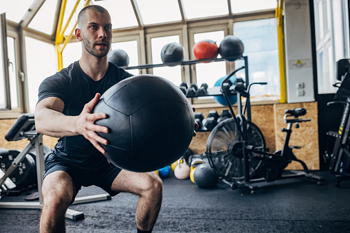 One man, fit man training with medicine ball in gym alone.
