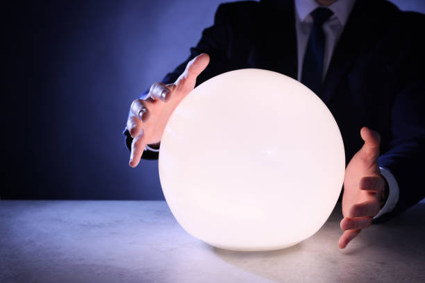istock Businessman using glowing crystal ball to predict future at table, closeup. Fortune telling 1434131857