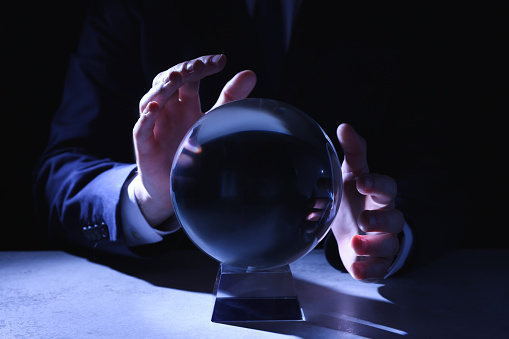 Businessman using crystal ball to predict future at table in darkness, closeup