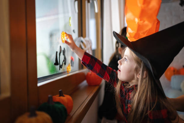 Petite fille déguisée en sorcière pour Halloween, décorant la fenêtre avec une décoration d’Halloween - Photo