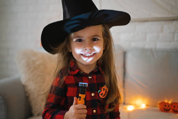 Caucasian toddler girl, dressed as a witch for a Halloween, holding flashlight stock photo