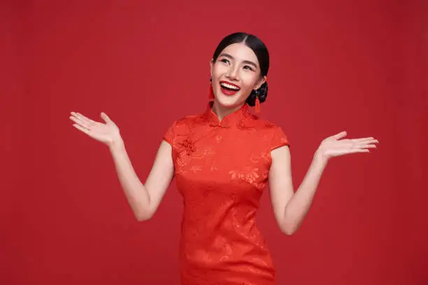 Happy Chinese new year. Asian woman wearing traditional cheongsam qipao dress with gesture of welcome isolated on red background.