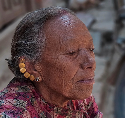 Kathmandu, Nepal - April 26, 2022: Close up of Nepali senior woman wearing many gold stud earrings the traditional way. Newari women use to wear sets of 