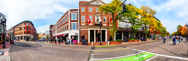 Cambridge, Massachusetts, USA - October 10, 2022: Panoramic view of the center of Harvard Square, the intersection of JFK Street, Brattle Street and Massachusetts Avenue during the Fall season. Across the street in the center is the Harvard Cooperative Society building flying the red \