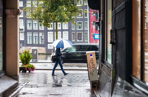 Amsterdam, Netherlands - A car passing a pedestrian on the street during a very wet morning in late summer in Amsterdam.
