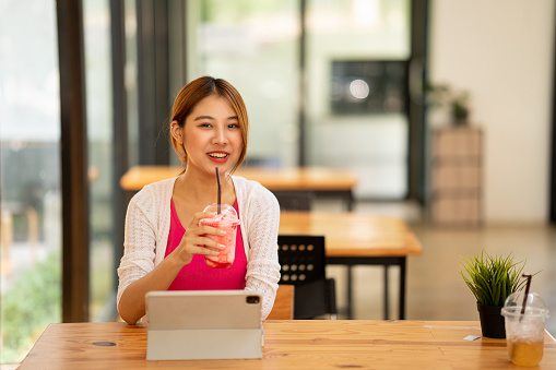 Asian female students studying online e-learning with tablet sitting at a desk and holding a pen distance learning concept at coffee shop