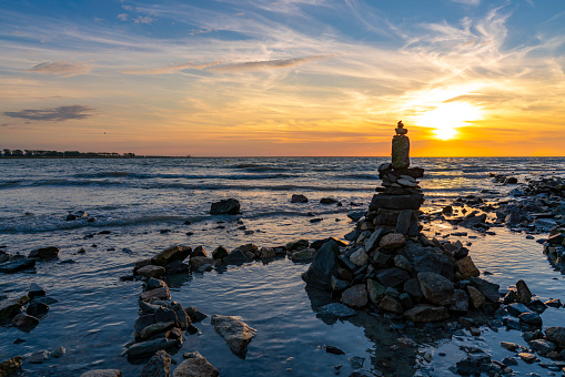 Cairn stacked stones in a sunset on the sea with horizon and golden blue sky on the dusk