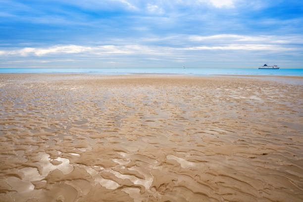 Calais beach France in low tide with wet sand dunes textures and Ferries to Dover on the sea.
