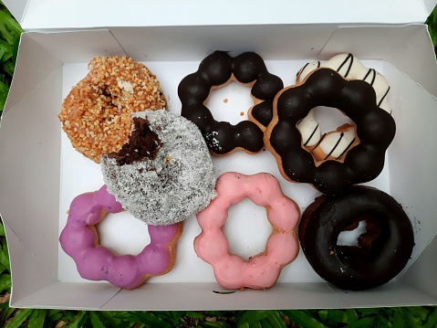 Assorted Bakery snacks and Donuts in paper box - green grass background.