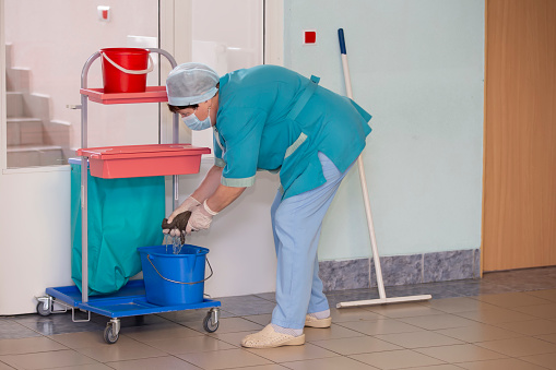 An adult female cleaner in uniform cleans the corridor of the hospital.