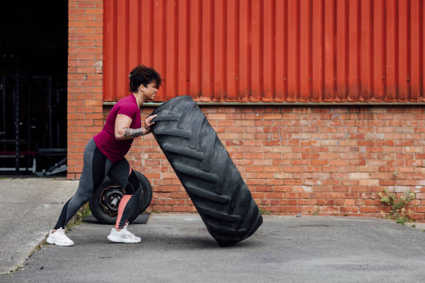 The Best Way to Train A woman pushing a truck tyre during a tyre workout at an outdoor gym in Newcastle upon Tyne, England. She is smiling while focusing on her strength. woman pushing tire stock pictures, royalty-free photos & images
