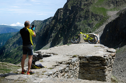 San Bernolfo, Italy - July 3, 2021: Cyclist making a photo with a smartphone of his mountain bike near the high pass of Colle Lounge, between italian and french Alps on july 3, 2021