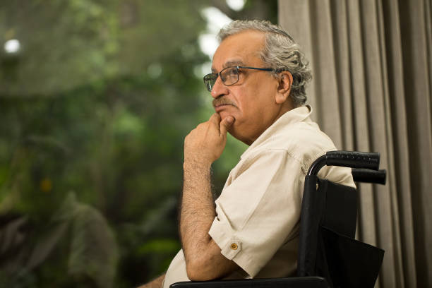 Disabled senior man on wheelchair in deep thoughts at home
