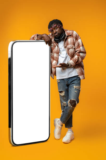 istock Smiling african man standing near huge smartphone with blank screen on yellow studio background 1434164175