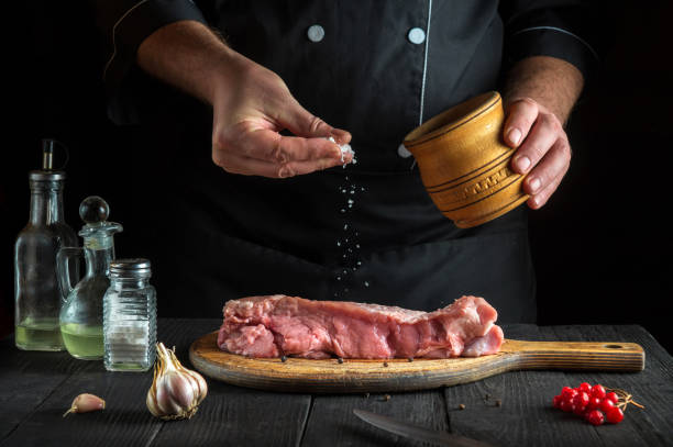 le chef prépare de la viande de veau crue. avant la cuisson, le chef ajoute du sel au bœuf. un plat national est en cours de préparation dans la cuisine du restaurant - veal calf meat baking photos et images de collection