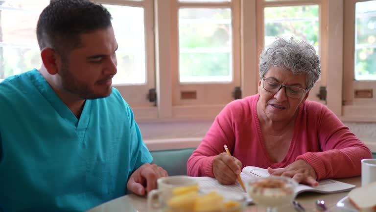 Mid adult nurse and senior woman playing with crosswords at home