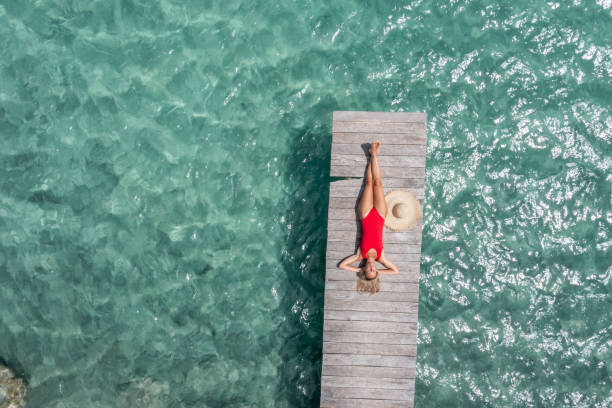 Drone view of woman relaxing on pier above lagoon stock photo