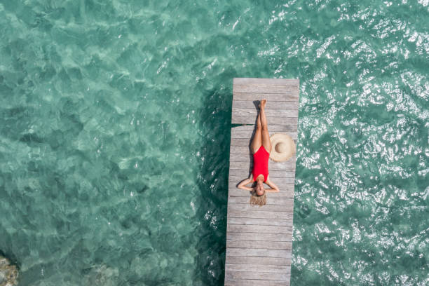 Drone view of woman relaxing on pier above lagoon 30's woman relaxes in nature on the beautiful lake of Bacalar, Mexico jetty aerial stock pictures, royalty-free photos & images