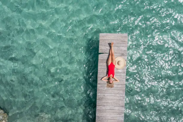 Photo of Drone view of woman relaxing on pier above lagoon