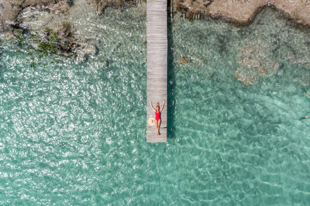 Drone view of woman relaxing on pier above lagoon 30's woman relaxes in nature on the beautiful lake of Bacalar, Mexico jetty aerial stock pictures, royalty-free photos & images