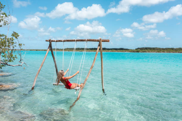 Drone view of Young woman having fun on swing in a beautiful lagoon on a sunny day View of woman swinging on white sand beach relaxing and sunbathing by the lagoon in Mexico swinger photo stock pictures, royalty-free photos & images
