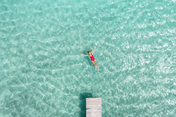 Drone view of woman floating on lagoon 30's woman relaxes in nature on the beautiful lake of Bacalar, Mexico jetty aerial stock pictures, royalty-free photos & images