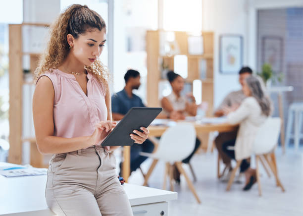 mujer de negocios, trabajando en tableta digital y oficina con colegas en colaboración reunidos en el fondo. empleada seria y enfocada en plan de marketing corporativo con tecnología. - break office 30s 20s fotografías e imágenes de stock