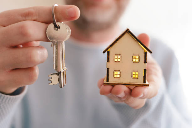 New home owner holding house keys and wooden model house stock photo