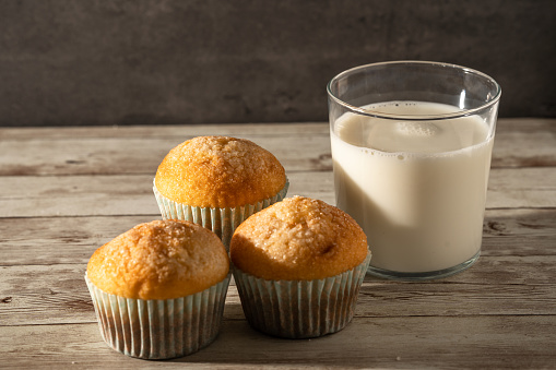 Glass of milk with three freshly baked muffins in the foreground - breakfast, snack, pastries concept