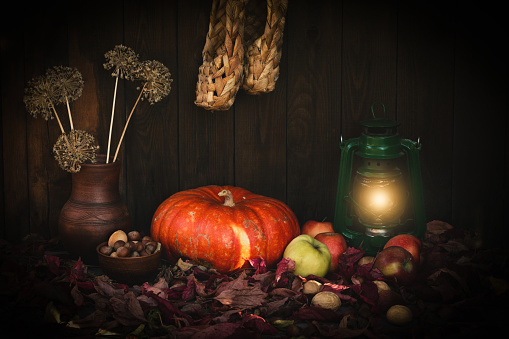 Autumn authentic rustic set on wooden backdrop with pumpkin, paraffin lamp, nuts, apples, clay jug, bast shoes, selective focus. Mabon, paganism, slavic tradition, Ukrainian folklore, thanksgiving.