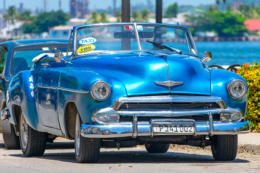 Havana, Cuba - September 16, 2022: Close-up of a blue convertible car parked by the side of the road. The vehicle has a taxi sign on the windshield, and another car is parked behind it.
