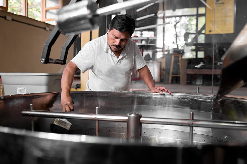 An Hispanic man is cleaning the coffee roaster machine cooling tray. Concept of local coffee production