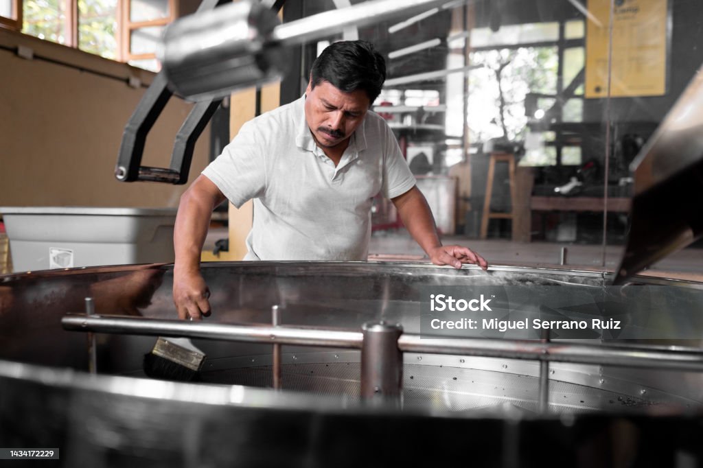An Hispanic man is cleaning the coffee roaster machine cooling tray An Hispanic man is cleaning the coffee roaster machine cooling tray. Concept of local coffee production Coffee Roaster Stock Photo