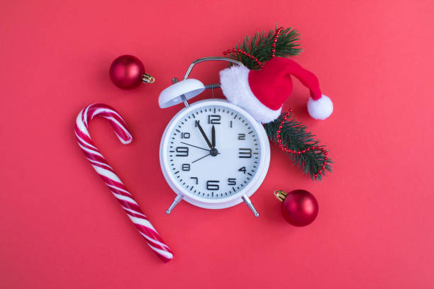 istock White alarm clock with Christmas Santa hat on the red background. Top view. Copy space. 1434173218